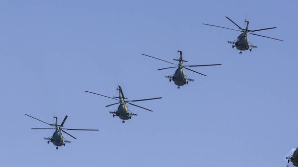 Διάφορα στρατιωτικά ελικόπτερα πετούν δίπλα-δίπλα ενάντια στον γαλάζιο ουρανό. - Φωτογραφία, εικόνα