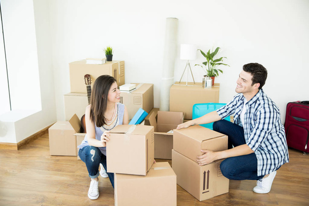 Happy man and woman in casuals crouching while stacking cardboard boxes in new home - Photo, image