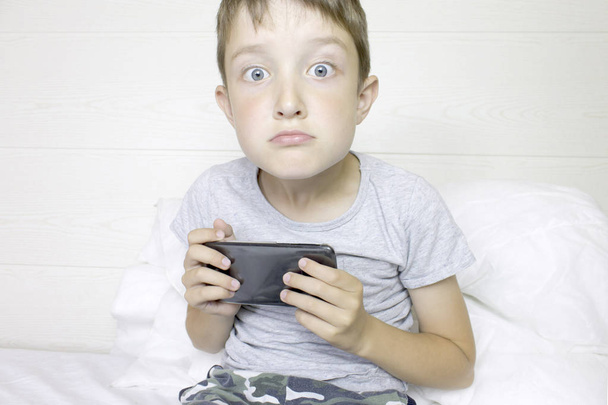Facial expessions of a young boy playing cellphone, smartphone device - Fotó, kép