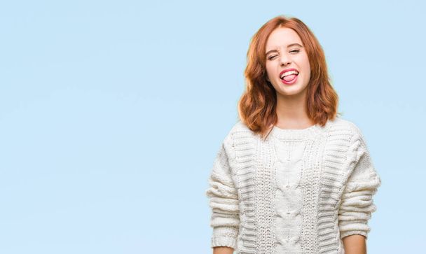 Young beautiful woman over isolated background wearing winter sweater sticking tongue out happy with funny expression. Emotion concept. - Zdjęcie, obraz