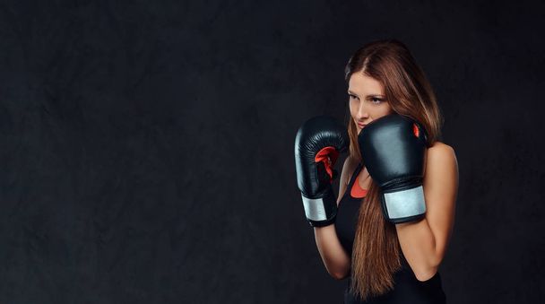 スタジオでポーズをとるボクシング グローブを身に着けているスポーツウェアを着て陽気な女性。ダーク テクスチャ背景に分離. - 写真・画像
