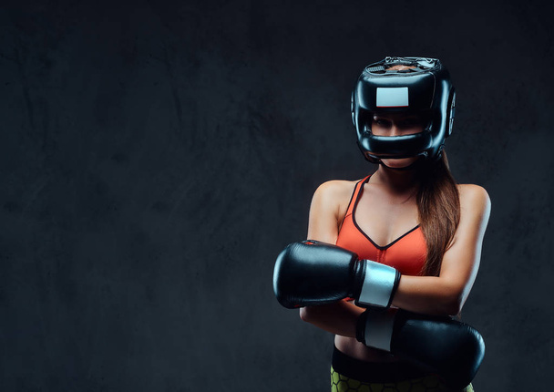 保護用のヘルメットとボクシング グローブ着用のスポーツブラで陽気な女性がスタジオでポーズします。ダーク テクスチャ背景に分離. - 写真・画像