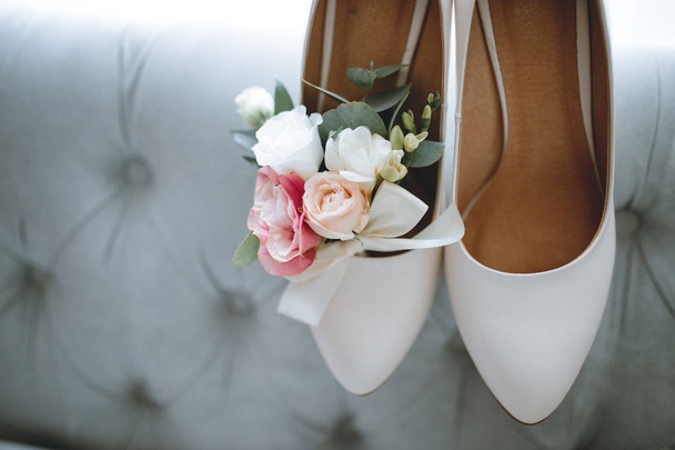 Brides wedding shoes with a bouquet with roses and other flowers on tha arm chair - Photo, Image