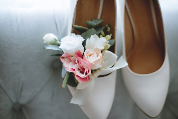 Brides wedding shoes with a bouquet with roses and other flowers on tha arm chair - Fotó, kép