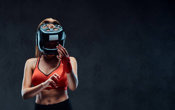 Porträt einer schönen brünetten Boxerin in Sport-BH bindet ihre Hände. isoliert auf dunklem, strukturiertem Hintergrund. - Foto, Bild