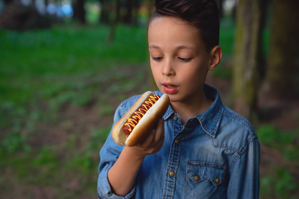 a young boy takes a bite of a hot dog - Фото, изображение