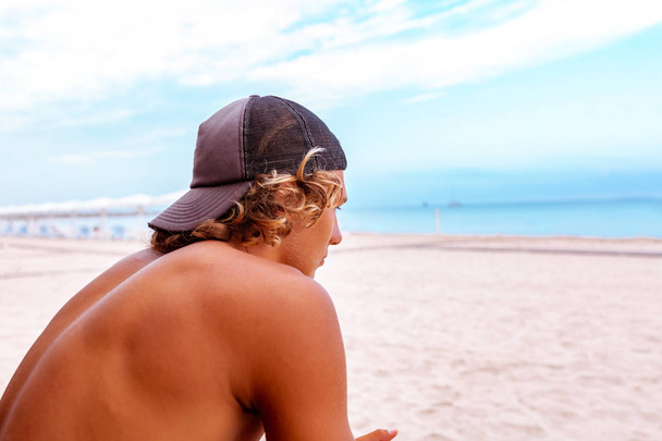 Серфер сидить спиною до камери на терасі на пляжі, дивлячись на відстань
, - Фото, зображення