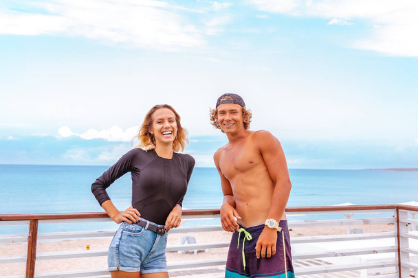 Hymyilevä nuori aktiivinen pari surffaajia rentouttava rannalla urheilun jälkeen
 - Valokuva, kuva