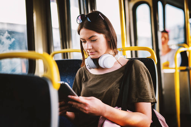 young adorable woman sitting on bus seat listening to music and drinking coffee  - 写真・画像