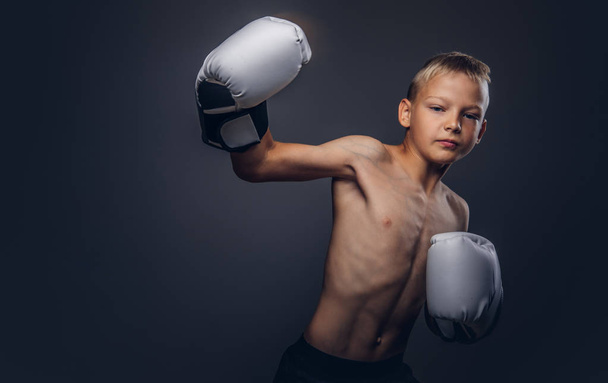Молодой боксер без рубашки с светлыми волосами в боксёрских перчатках показывает боксёрский крючок
. - Фото, изображение
