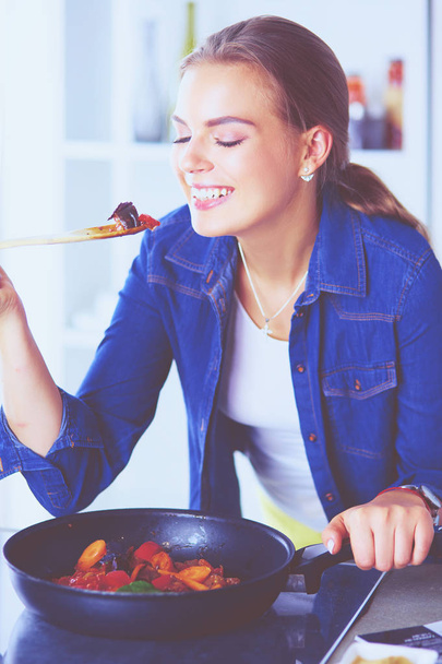 Young woman cooking healthy food holding a pan with vegetables is it. Healthy lifestyle, cooking at home concept - Foto, afbeelding