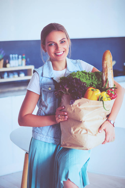 Young woman holding grocery shopping bag with vegetables .Standing in the kitchen - Foto, immagini