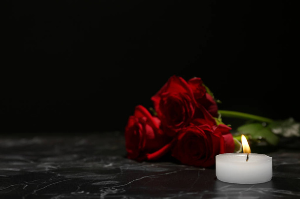 Beautiful red roses and candle on table against black background. Funeral symbol - Foto, immagini