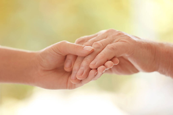 Young woman holding elderly man hand on blurred background, closeup. Help service - Photo, Image