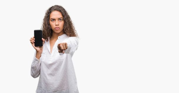 Jeune femme hispanique à l'aide d'un smartphone pointant du doigt vers la caméra et vers vous, signe de la main, geste positif et confiant de l'avant
 - Photo, image