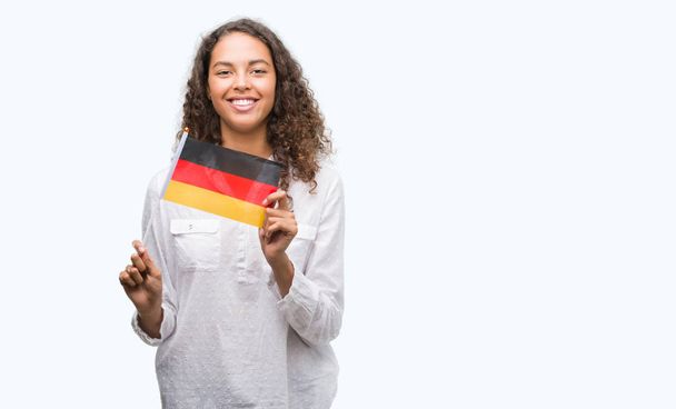 Young hispanic woman holding flag of Germany with a happy face standing and smiling with a confident smile showing teeth - Fotografie, Obrázek