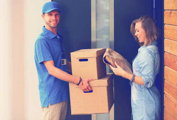 Uomo di consegna sorridente in uniforme blu che consegna pacchi al destinatario concetto di servizio di corriere. Uomo sorridente consegna in uniforme blu - Foto, immagini