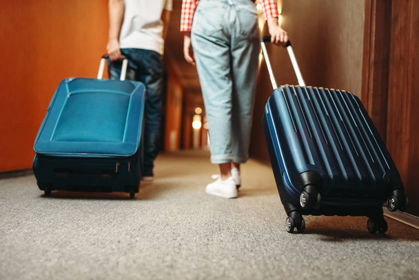 Couple with suitcases walking by the hotel corridor. Travelling or tourism concept. Tourists with bags in hallway - Photo, Image