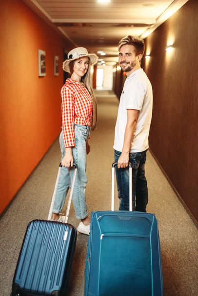 Pareja sonriente con maletas en el pasillo del hotel. Concepto de viaje o turismo. Viajeros con maletas en pasillo
 - Foto, Imagen