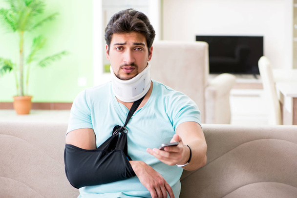 Jeune étudiant homme avec cou et blessure à la main assis sur le canapé - Photo, image