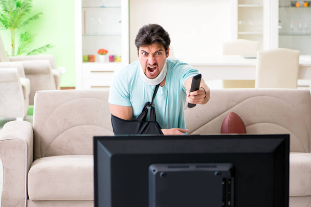 Человек с травмой шеи и руки смотрит американский футбол по телевизору - Фото, изображение
