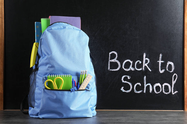 Backpack with stationery on table against blackboard with written words BACK TO SCHOOL - Foto, immagini