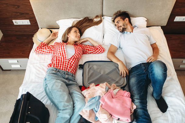 Couple lies on the bed with opened suitcase, top view - Photo, Image