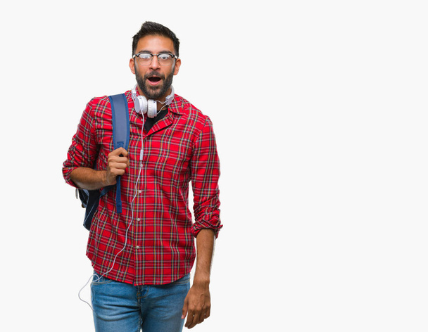 Adult hispanic student man wearing headphones and backpack over isolated background afraid and shocked with surprise expression, fear and excited face. - 写真・画像