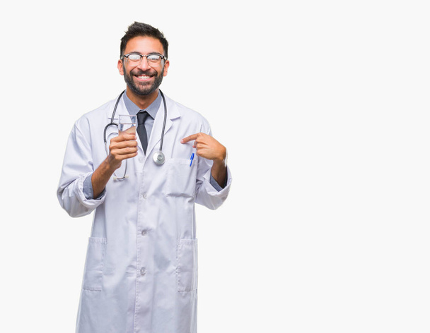 Взрослый латиноамериканец-врач пьет воду на изолированном фоне с удивленным лицом, указывающим пальцем на себя
 - Фото, изображение
