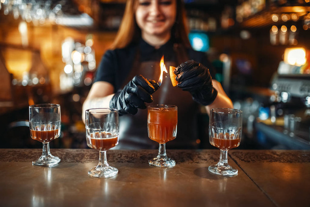 Barkeeperin macht Koktail mit dem Feuer. Zubereitung alkoholischer Getränke. Barmann arbeitet an der Theke in Kneipe - Foto, Bild