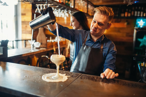 Male barman pouring the drink from the shaker at the bar counter. Alcoholic coctail preparation. Barkeeper occupation, bartending - Photo, Image