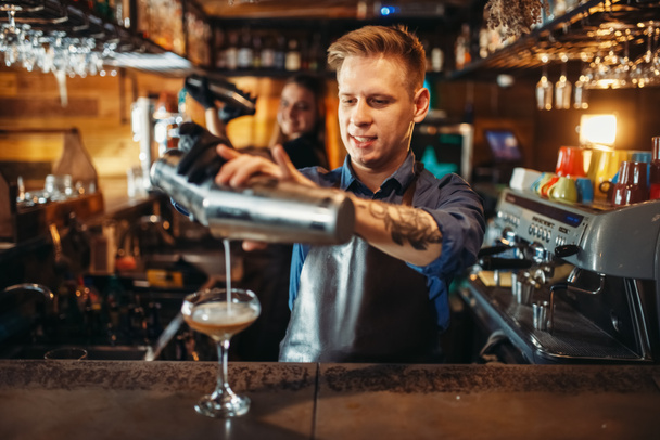Hombre barman vertiendo la bebida de la coctelera en el mostrador del bar. Preparación de cócteles alcohólicos. Ocupación de camarero, camarero
 - Foto, imagen