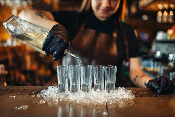 Mulher barman em luvas coloca bebidas no gelo. Mulher barman a misturar-se no balcão do bar no pub. Ocupação de empregado
 - Foto, Imagem