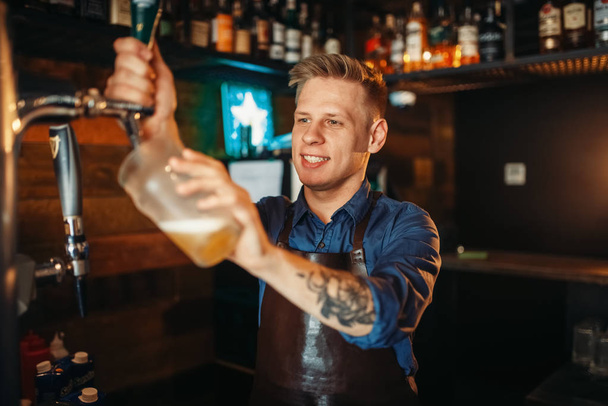 Αρσενικό μπάρμαν έκχυση μπίρα στο μπαρ του μετρητή. Επάγγελμα μπάρμαν, bartending - Φωτογραφία, εικόνα