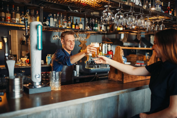Męski barman przechodzi szklanki piwa do kobiety gościem. Barman zawód, barman i kobieta w barze licznika - Zdjęcie, obraz