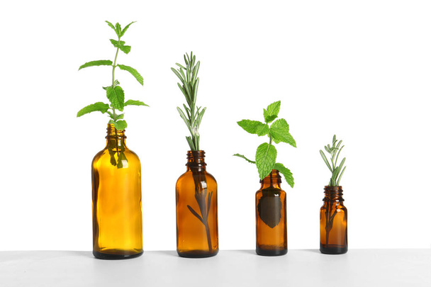 Row of glass bottles with rosemary and mint on white background - Foto, afbeelding