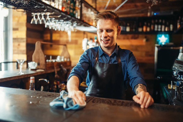 Mannelijke barman in schort reinigt toog. Bezetting van de barkeeper, barman zet orde op zaken - Foto, afbeelding