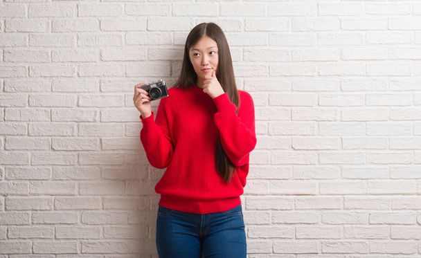 Tuğla duvar holding vintage kamera ciddi bir yüz düşünme hakkında soru, çok karışık fikir genç Çinli kadın - Fotoğraf, Görsel