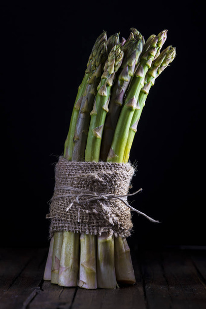 Asparagus bundle on a black background wrapped with a piece of burlap - Фото, зображення