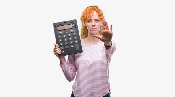 Genç Kızıl saçlı kadın holding büyük hesap makinesi açık eliyle dur işareti ile ciddi ve kendine güvenen ifade, savunma hareketi yapıyor - Fotoğraf, Görsel