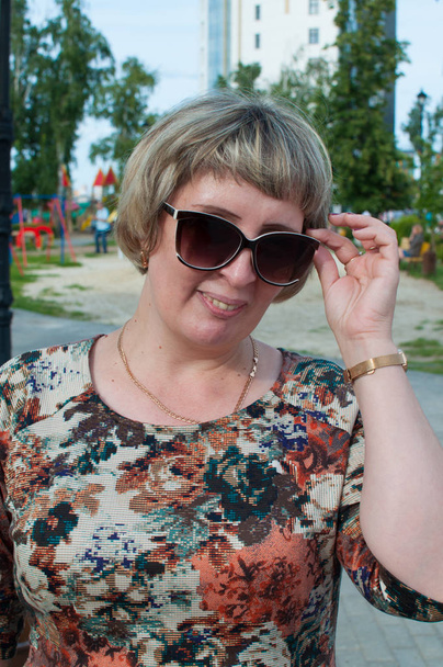 The Russian woman in sunglasses walks in the park in the summer - Фото, изображение
