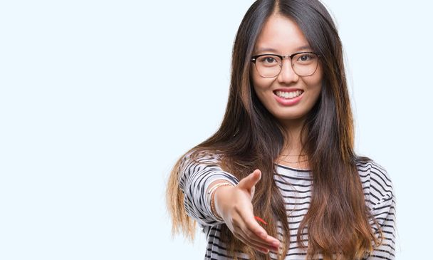 Young asian woman wearing glasses over isolated background smiling friendly offering handshake as greeting and welcoming. Successful business. - Foto, Bild
