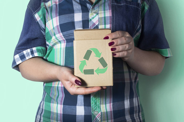 Naisen käsissä on pahvilaatikko, jossa on kierrätyssymboli. Kierrätys, ympäristö ja ekologia
. - Valokuva, kuva
