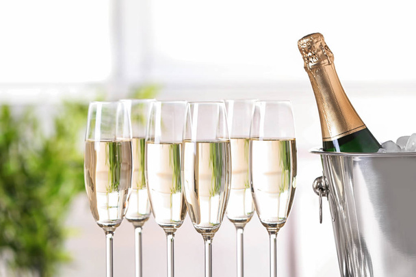 Glasses with champagne and bottle in bucket against blurred background - Foto, Imagen