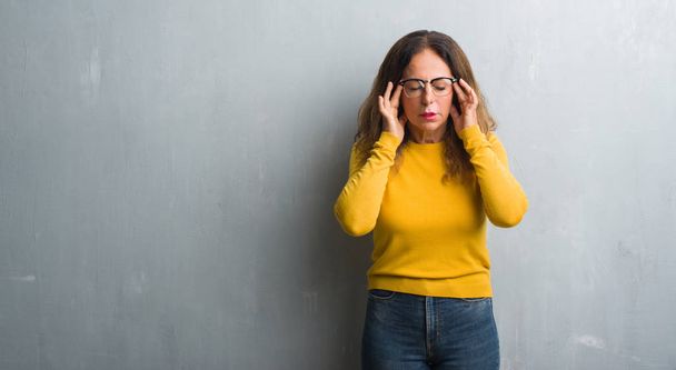 Middle age hispanic woman over grey wall wearing glasses with hand on head for pain in head because stress. Suffering migraine. - Φωτογραφία, εικόνα