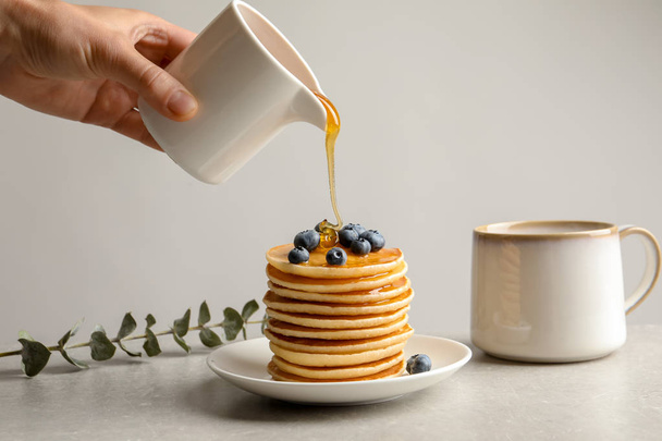 Woman pouring honey onto tasty pancakes with berries on table, closeup - Foto, Imagem