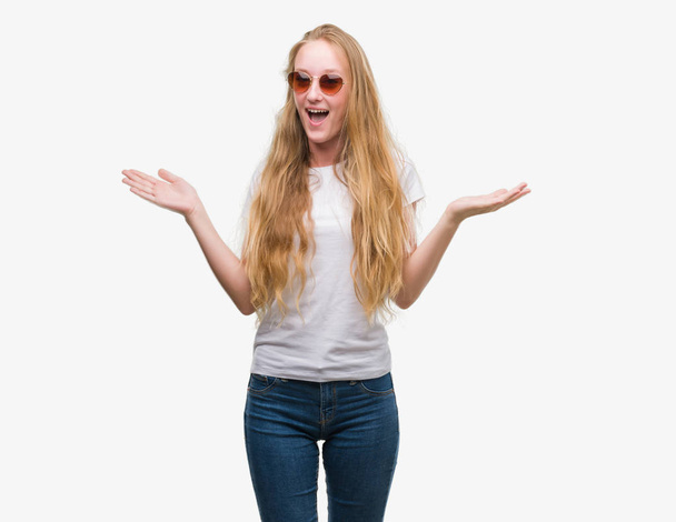 Блондинка-подросток в солнцезащитных очках очень счастливая и взволнованная, победительница, празднующая победу кричит с большой улыбкой и поднятыми руками
 - Фото, изображение