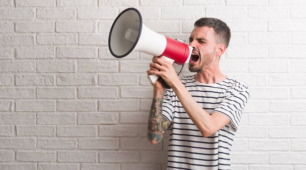 Joven hombre adulto sosteniendo megáfono molesto y frustrado gritando con ira, loco y gritando con la mano levantada, concepto de ira
 - Foto, imagen