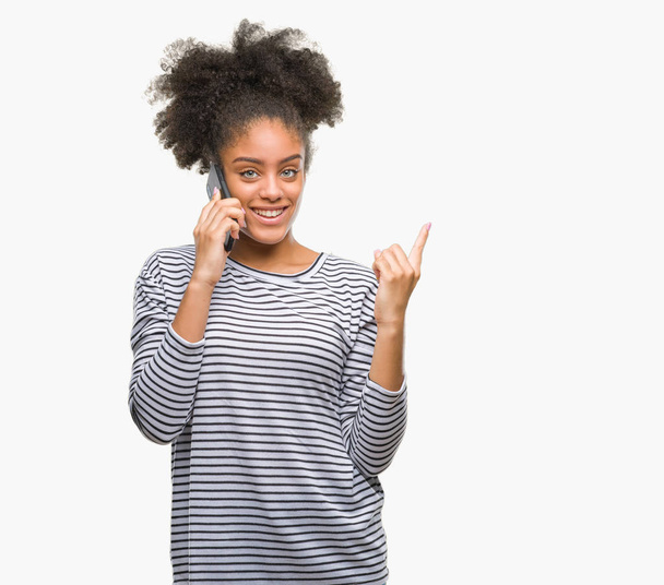 Young afro american woman talking on the phone over isolated background very happy pointing with hand and finger to the side - Fotoğraf, Görsel