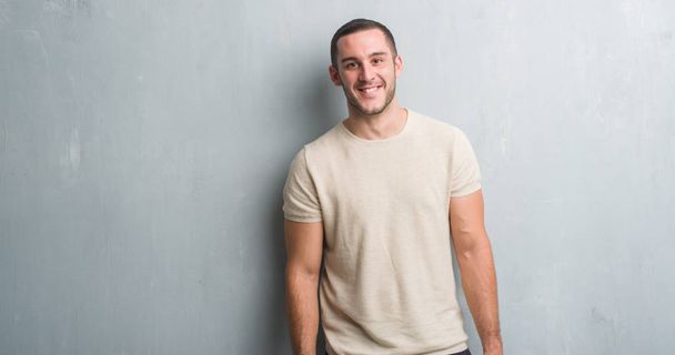 Young caucasian man over grey grunge wall with a happy face standing and smiling with a confident smile showing teeth - Photo, Image
